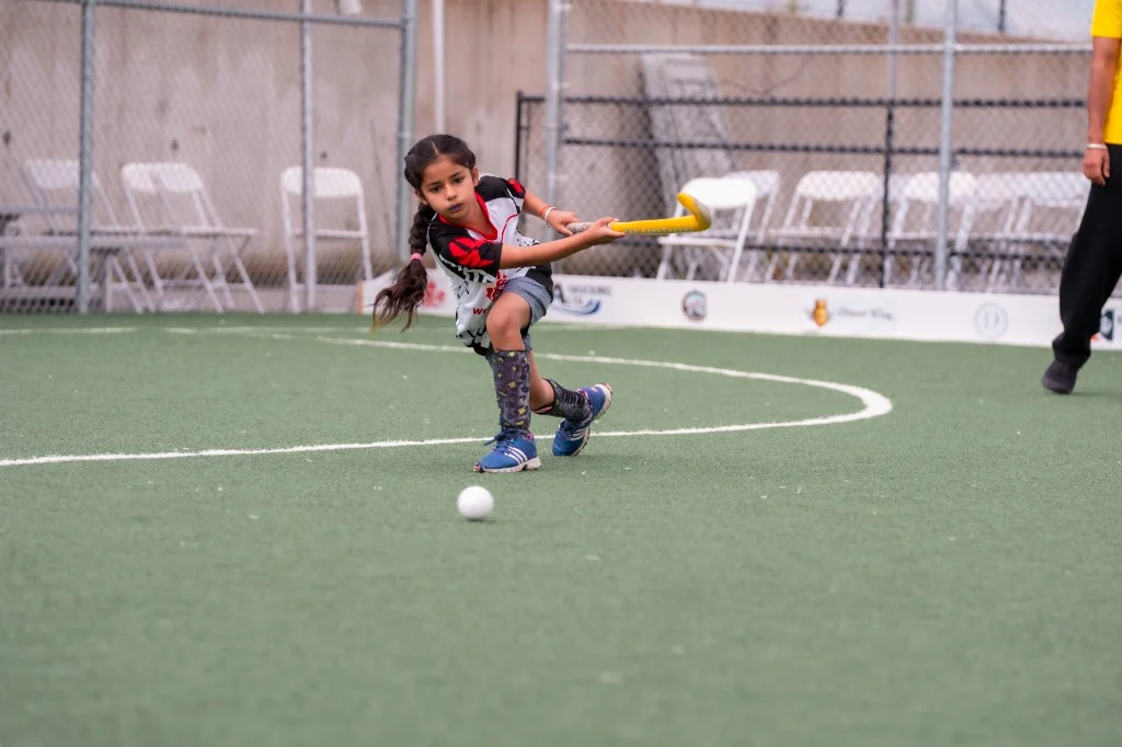 Young Wolverines athlete delivering a low sweeping shot on turf